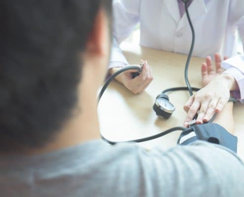 A healthcare professional measures a patients blood pressure with a sphygmomanometer at a desk.