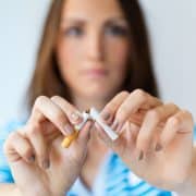 A woman in a blue-striped shirt breaks a cigarette in half with both hands, with her face out of focus in the background.