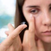 A person holds a contact lens on their fingertip, preparing to insert it into their eye.