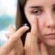 A person holds a contact lens on their fingertip, preparing to insert it into their eye.