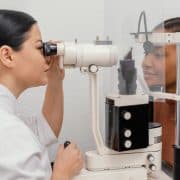 An eye care professional examines a patients eye using a slit lamp during an eye check-up. Both are separated by a clear plastic divider.