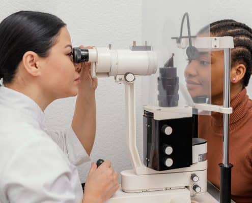 An eye care professional examines a patients eye using a slit lamp during an eye check-up. Both are separated by a clear plastic divider.